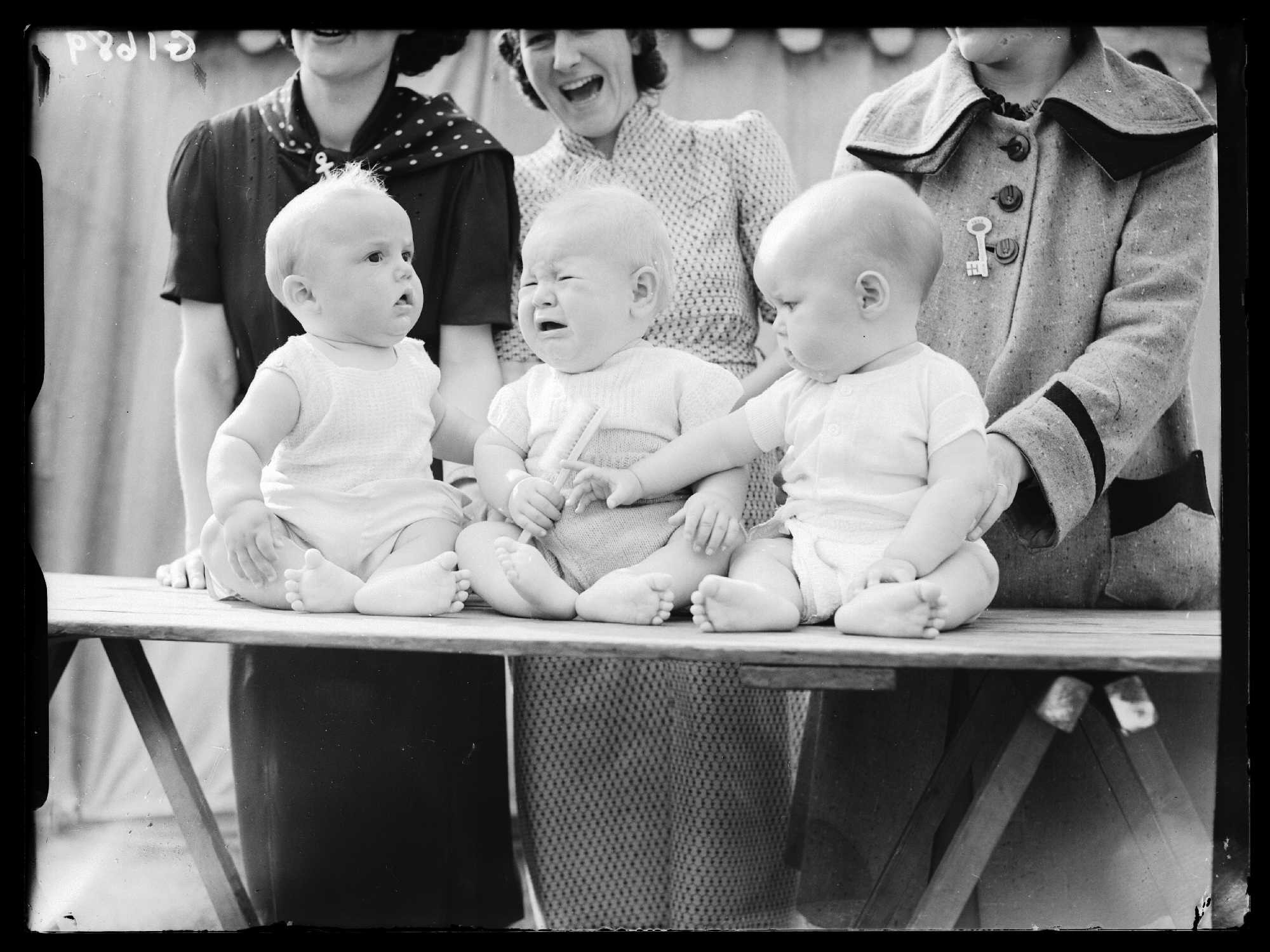 Three babies sitting in front of a crowd