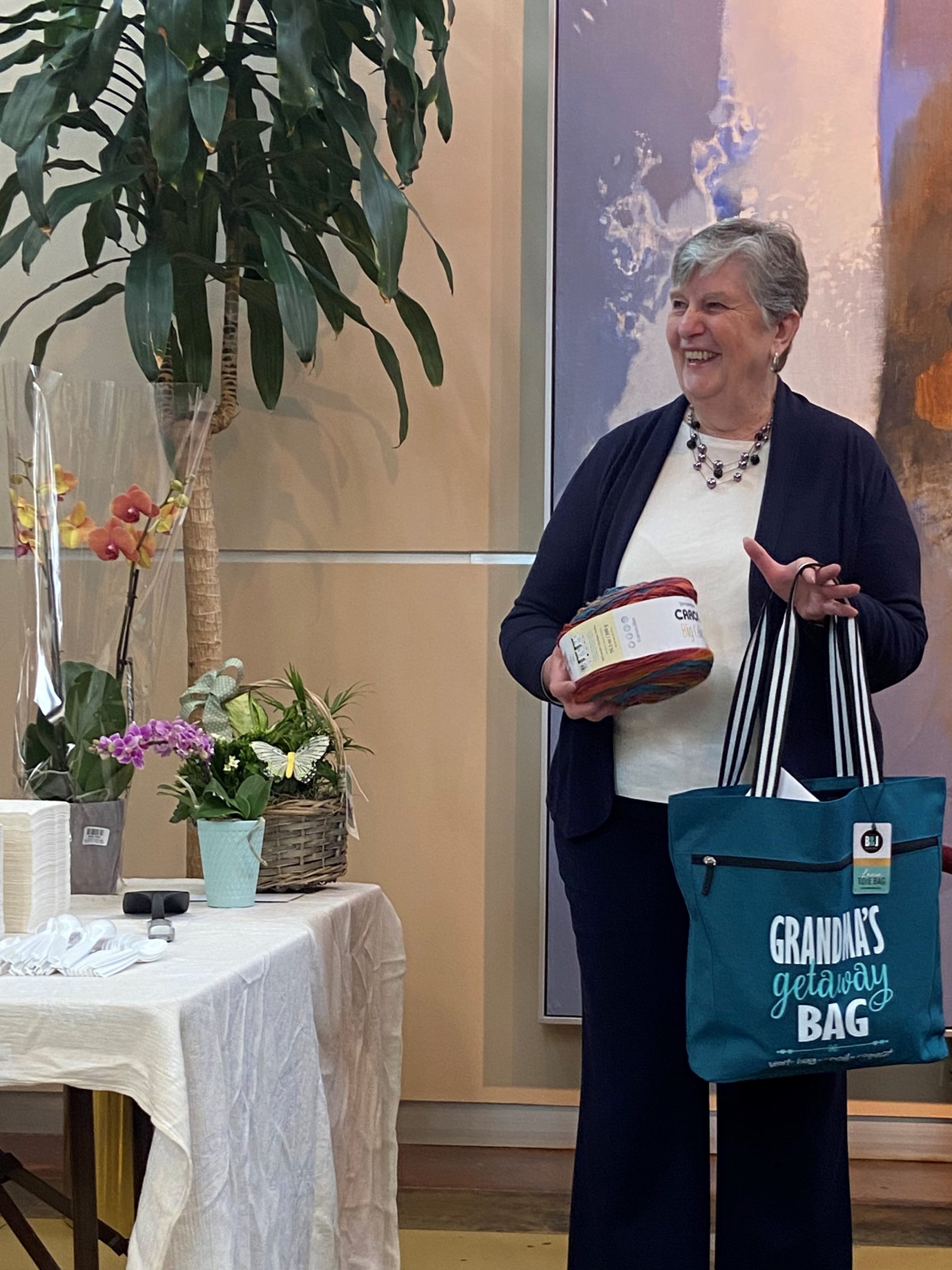 Rosemary standing at her retirement party holding gifts including a big that says "Grandma's Getaway Bag"