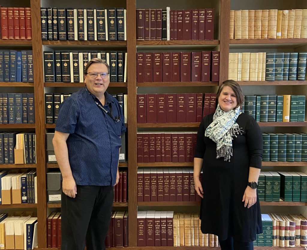 Reference Archivists Tony Castro and Heidi Stringham stand in front of a large bookshelf in the new Reference Room.
