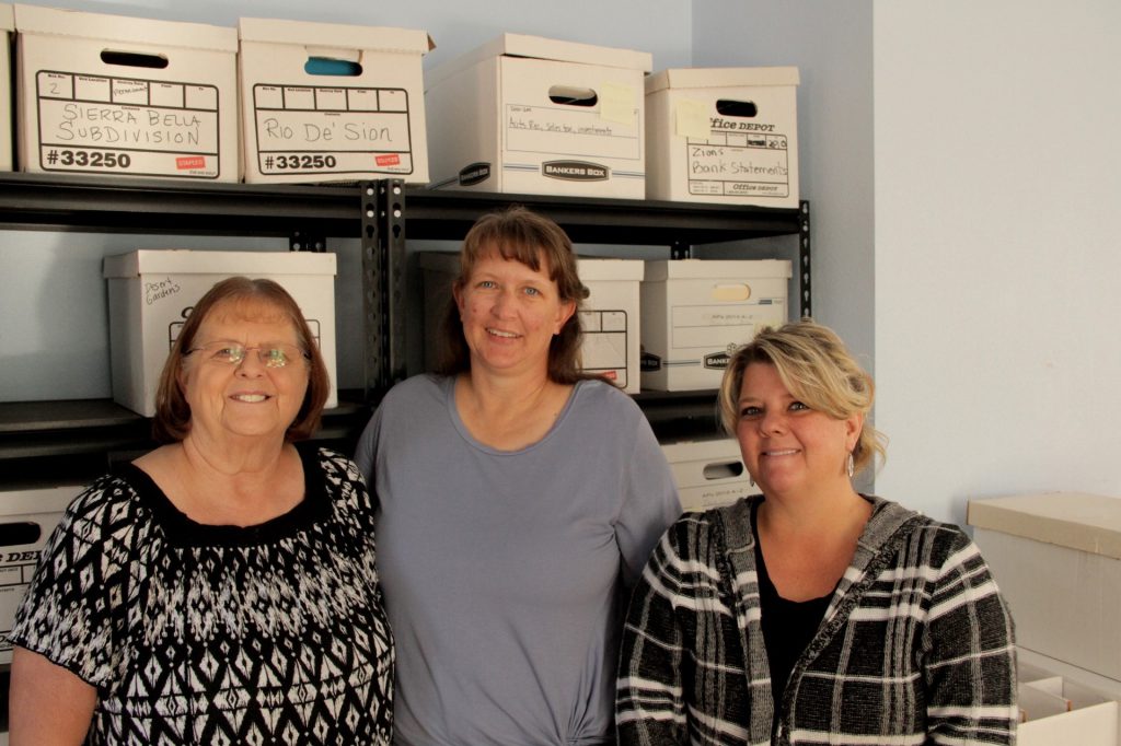 Three women in front of file boxes 